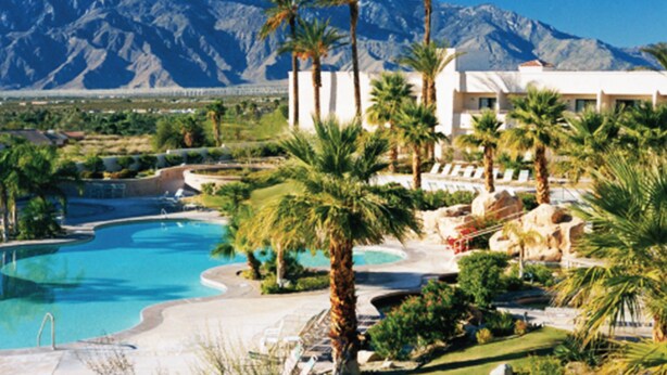 Un resort con piscina, palmeras y una montaña al fondo.