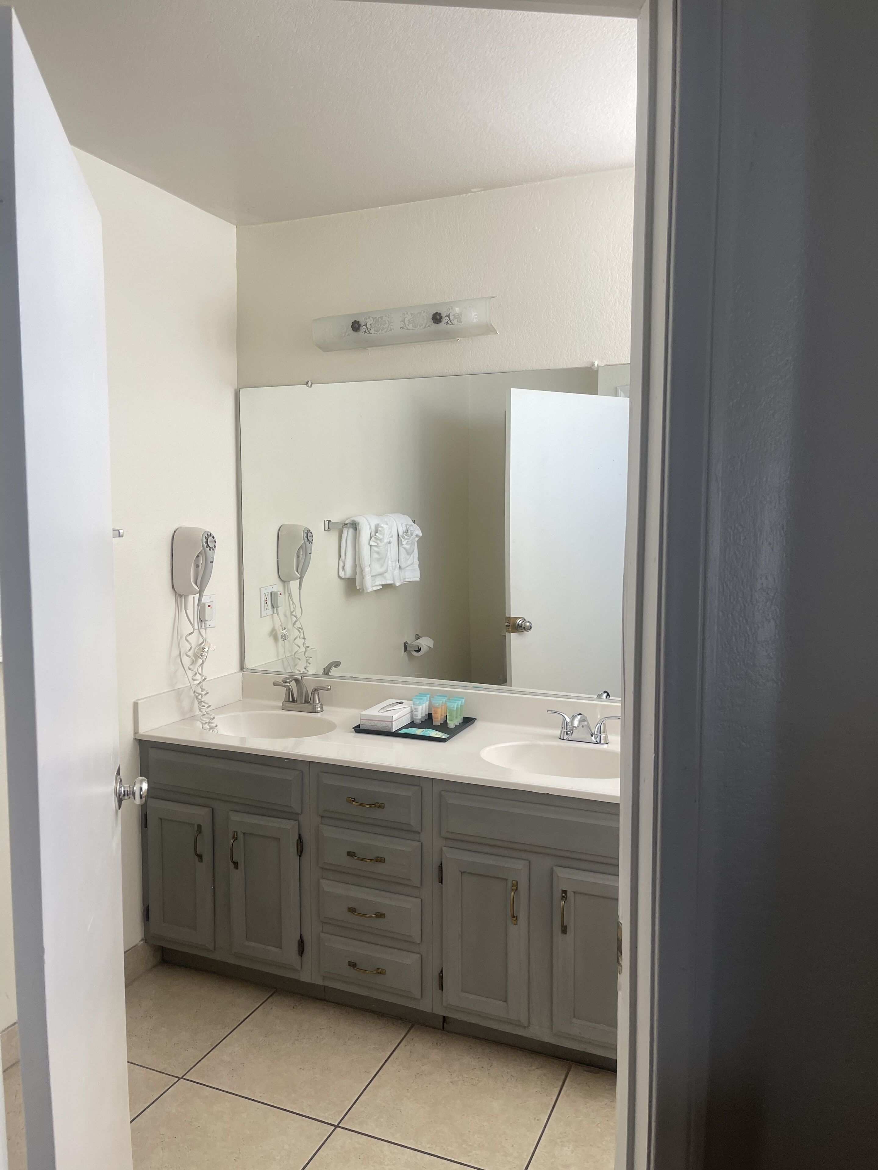 A bathroom with a double sink vanity, a large mirror, and a hairdryer on the wall.