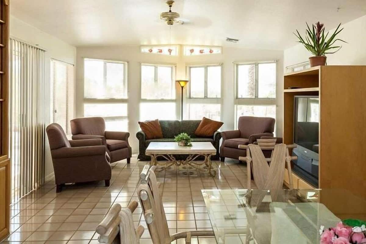 Un salon avec deux fauteuils marron, un canapé vert, une table basse en verre et un téléviseur posé sur un meuble en bois.