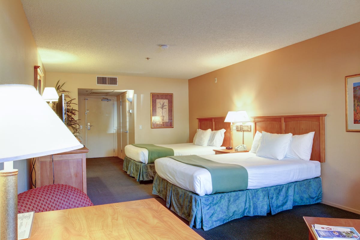 Une chambre d’hôtel avec deux lits, un bureau, une chaise, une lampe et une porte donnant sur une salle de bain.