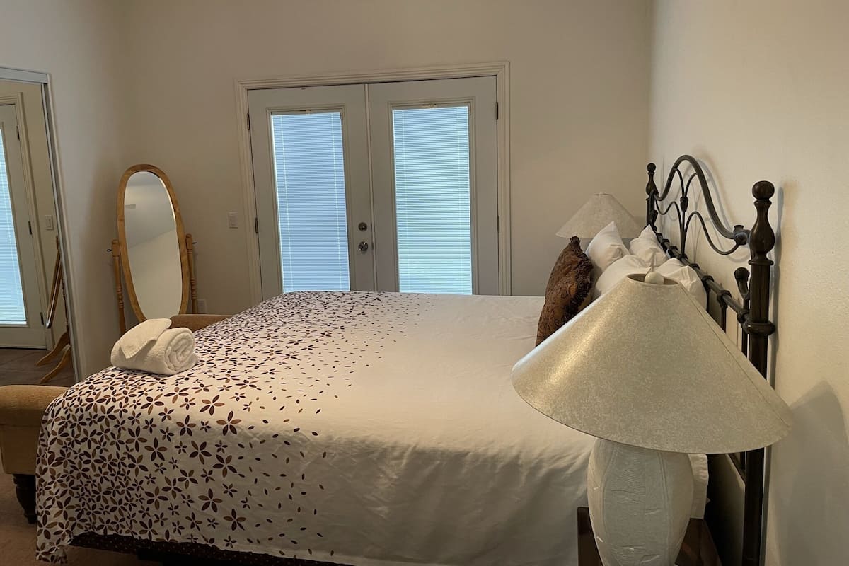 Une chambre à coucher avec un lit, une lampe de chevet, un miroir et une porte avec des stores.