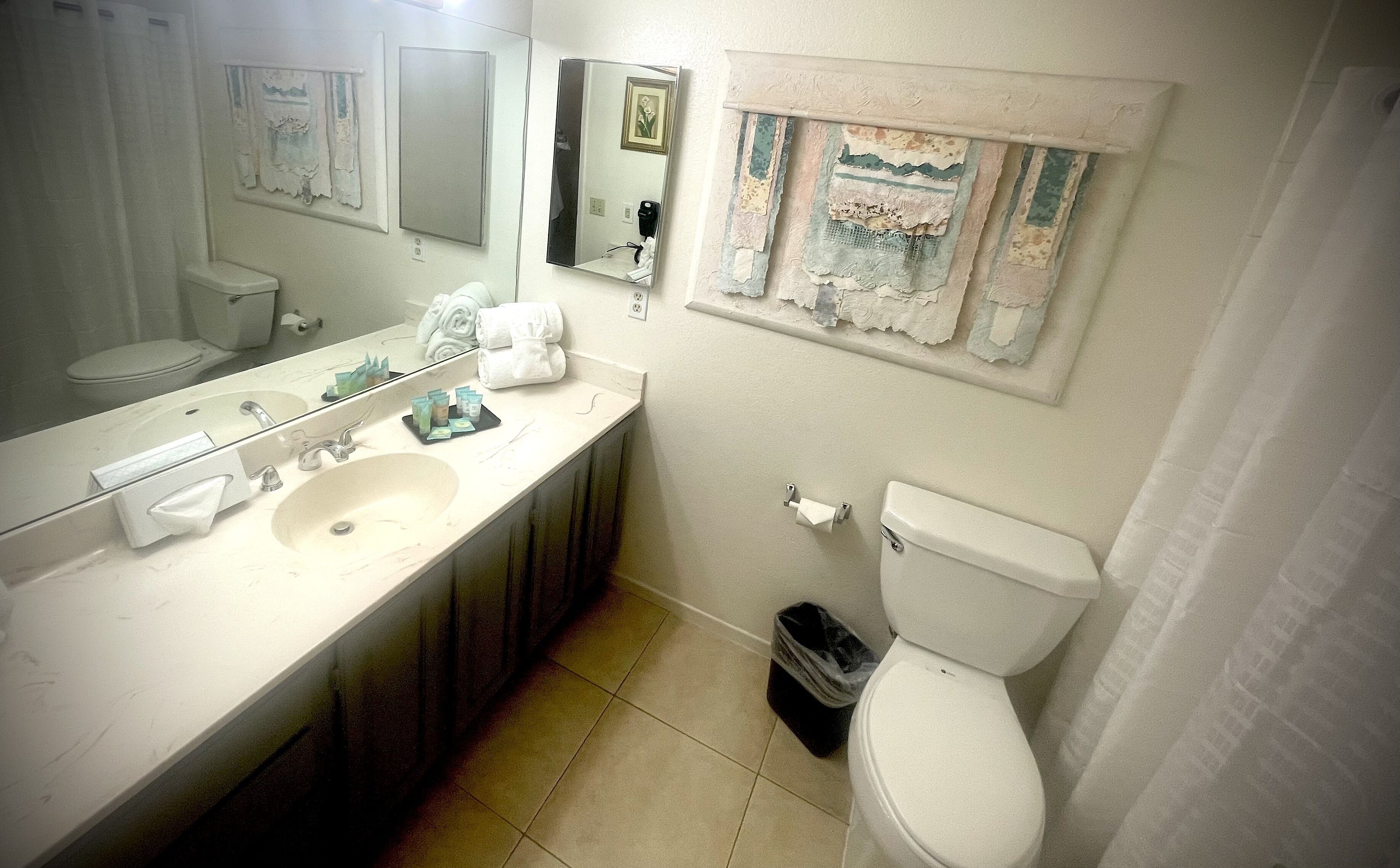 A bathroom with a white sink, mirror, and toilet. There are towels and toiletries on the counter.
