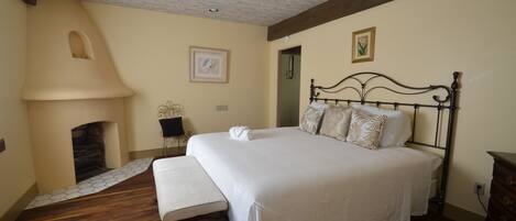 A bedroom with a large bed, a bench, a fireplace, and a ceiling fan.