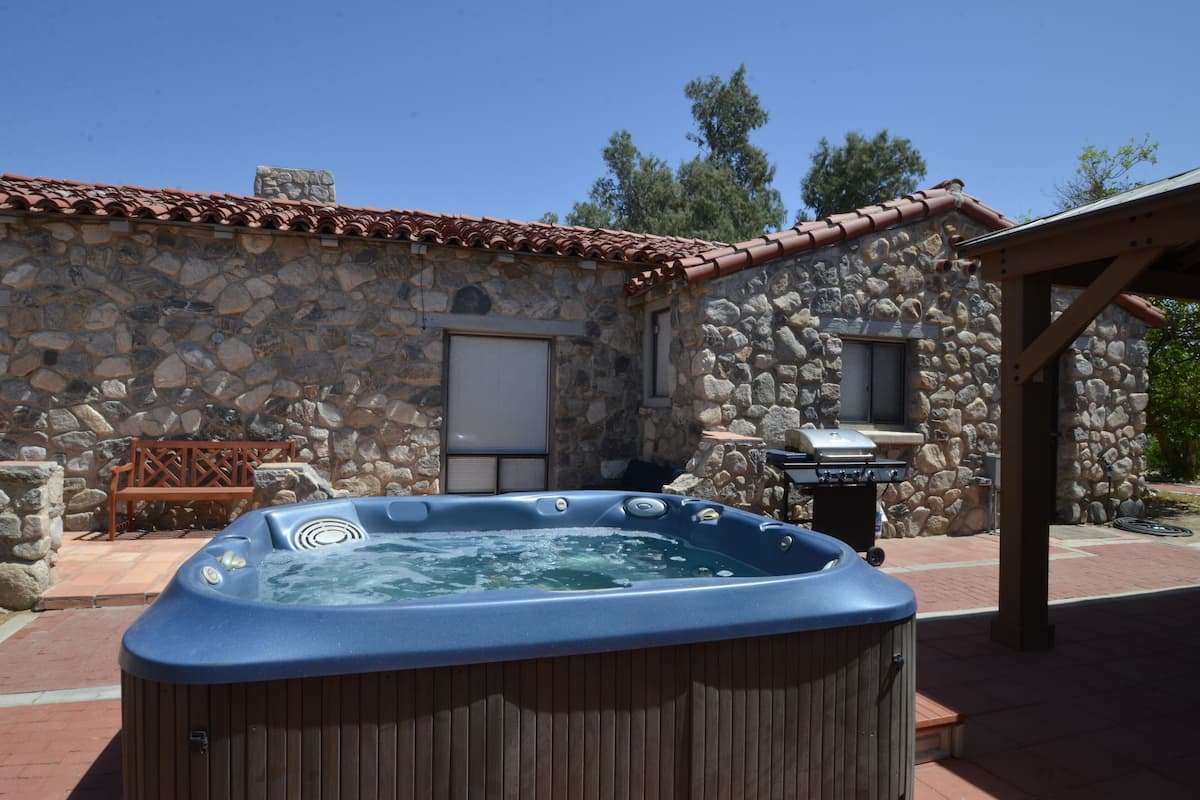 Un bâtiment en pierre doté d’un jacuzzi, d’un espace barbecue et d’un banc en bois.