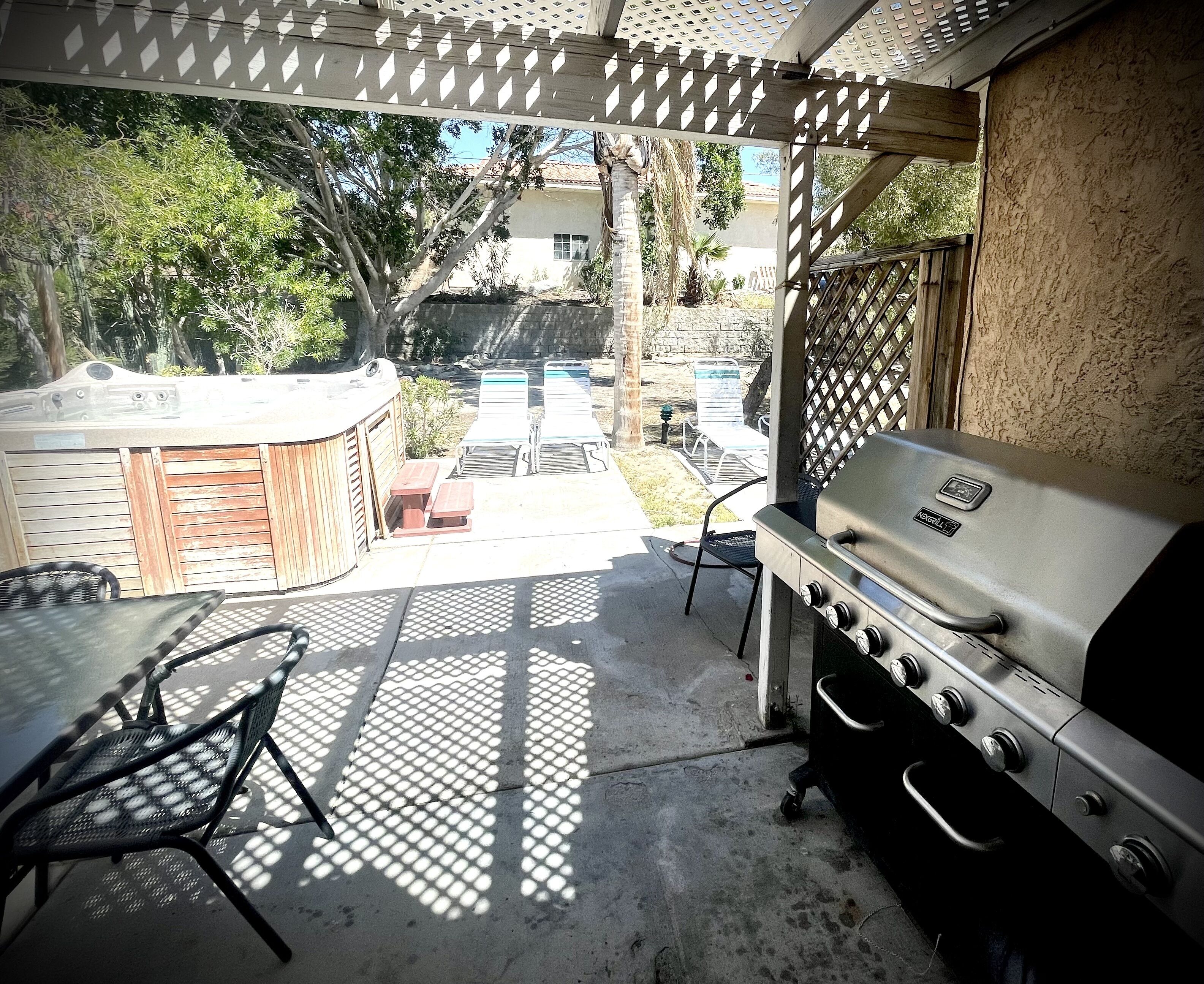 An outdoor patio with a grill, a hot tub, and a covered seating area.