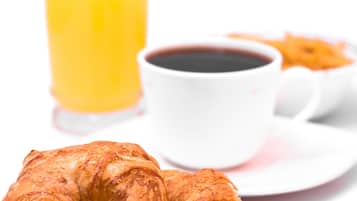 Un croissant sur une assiette, une tasse de café et un verre de jus d’orange.