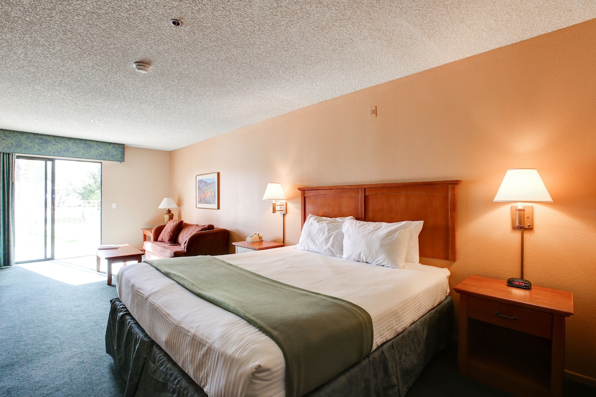Une chambre d’hôtel avec un grand lit, deux tables de chevet avec des lampes, une tête de lit en bois et une vue sur l’extérieur grâce à une porte coulissante.