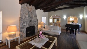 Una sala de estar acogedora con chimenea de piedra, un piano, un sofá y una mesa de centro con objetos decorativos.