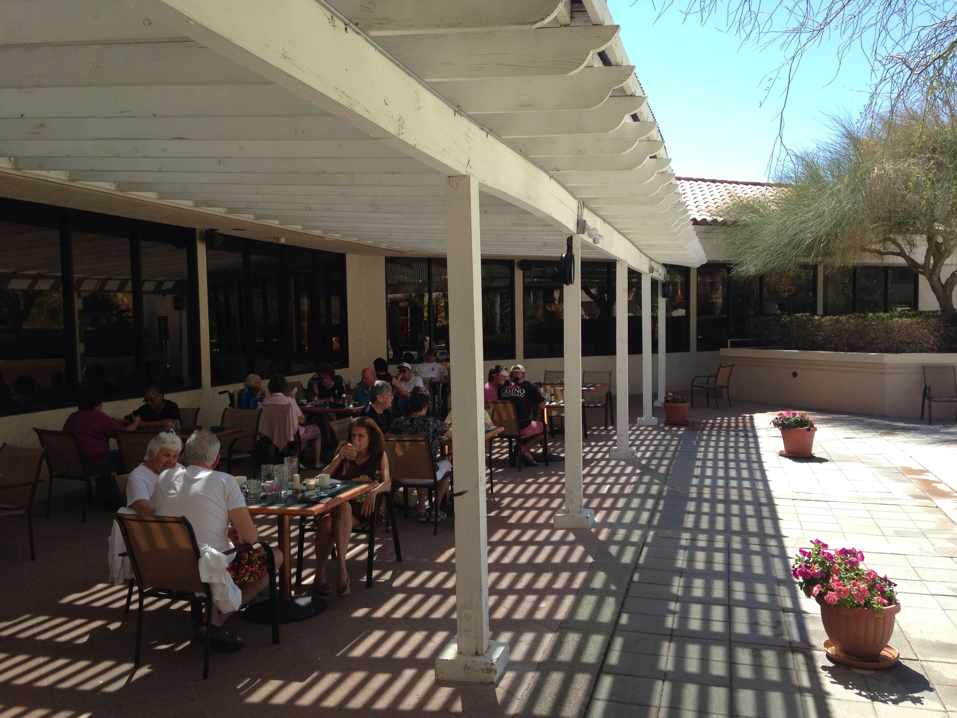 An outdoor patio with tables and chairs, large windows, and a pergola structure.