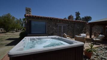 Un jacuzzi en un patio trasero con muros de piedra, sillas de mimbre y una planta en maceta.
