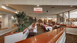 Un interior de restaurante con una barra larga, varias mesas y plantas en macetas.