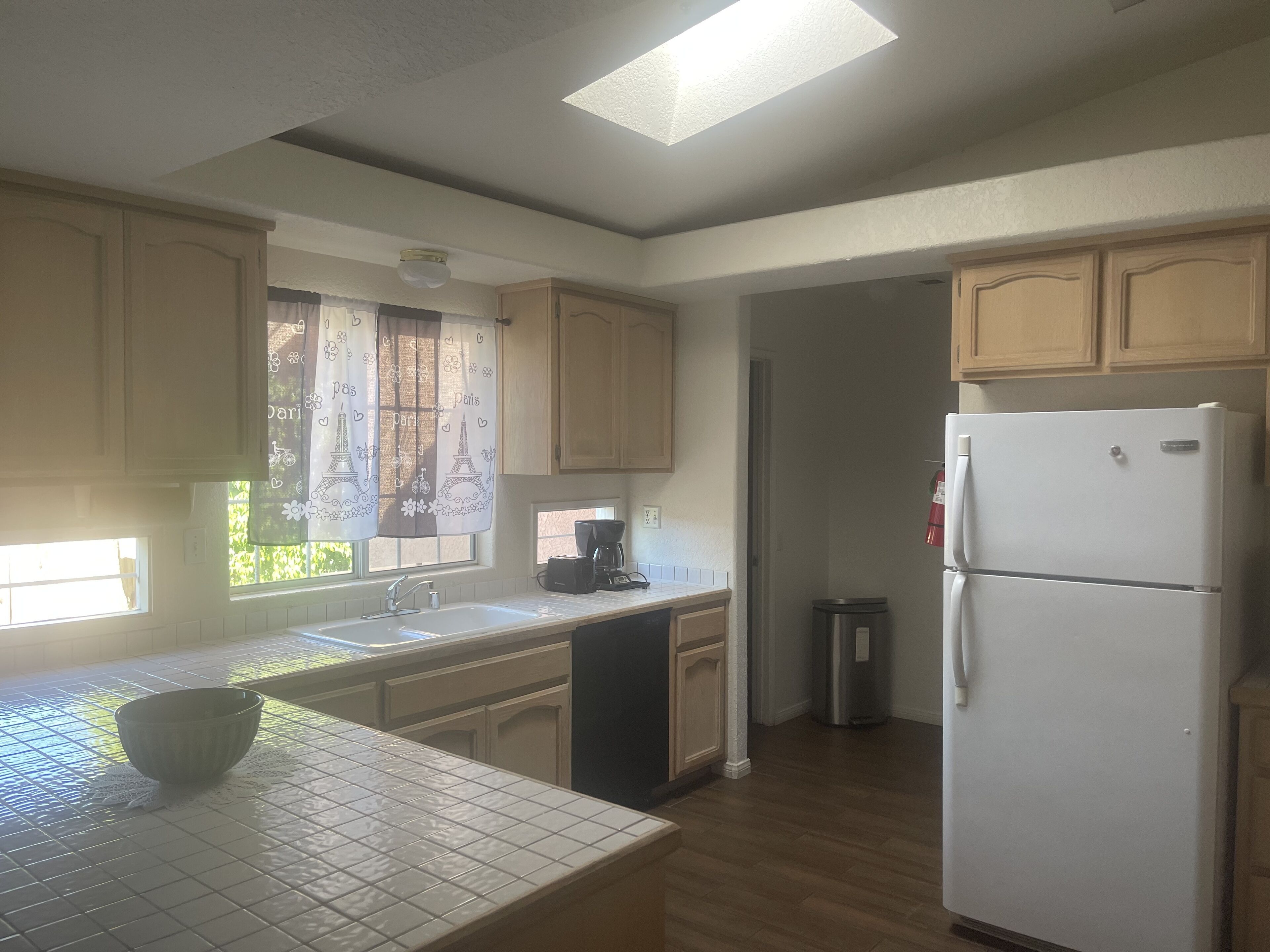 A kitchen with wooden cabinets, a white refrigerator, a coffee maker, and a window with a curtain.