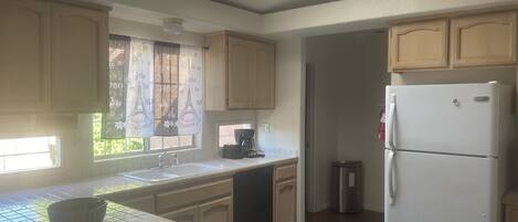 A kitchen with wooden cabinets, a white refrigerator, a coffee maker, and a window with a curtain.