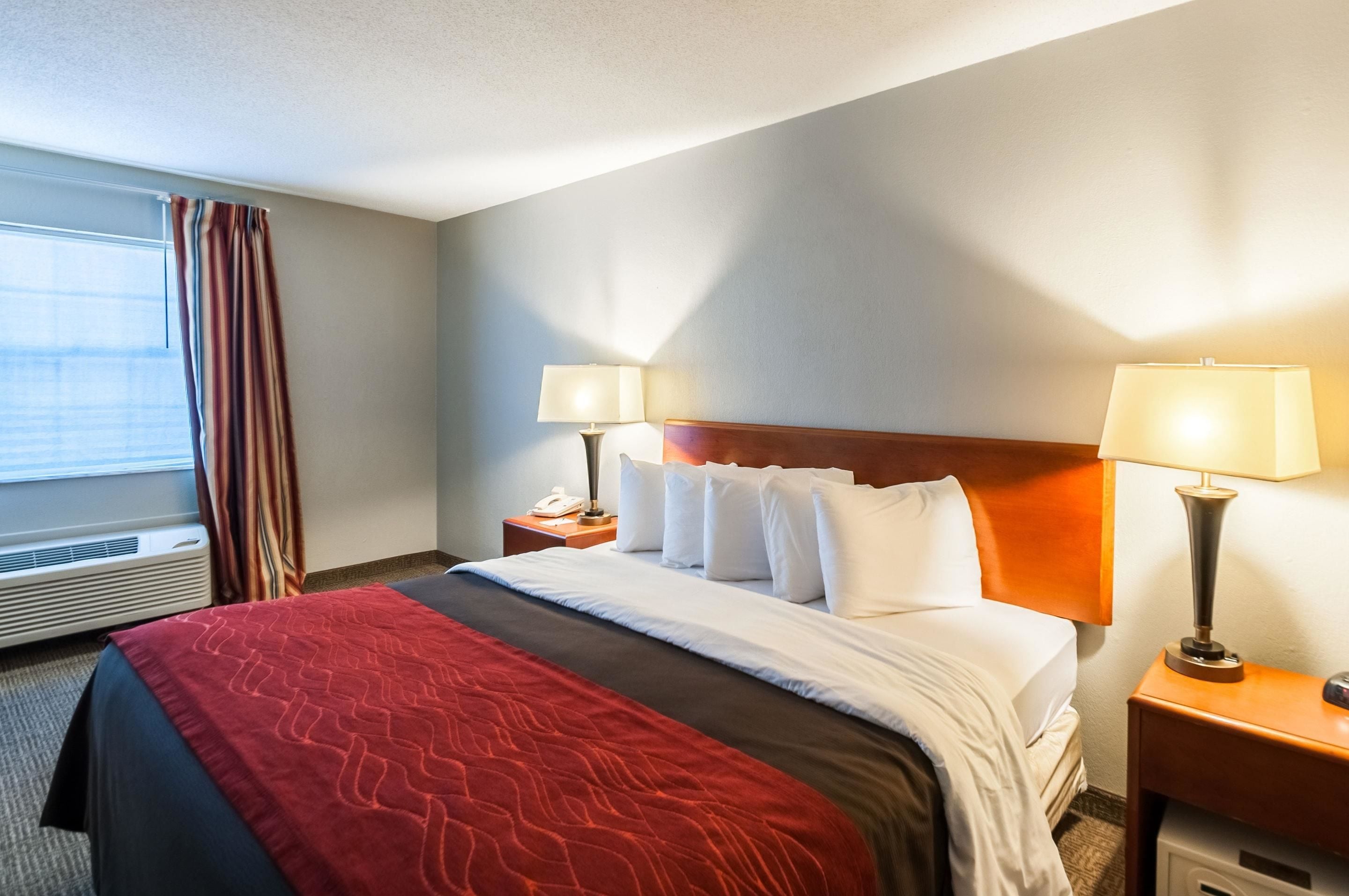 Habitación de hotel con cama, dos mesitas de noche, una lámpara en cada una, ventana con cortinas e instalación de aire acondicionado.