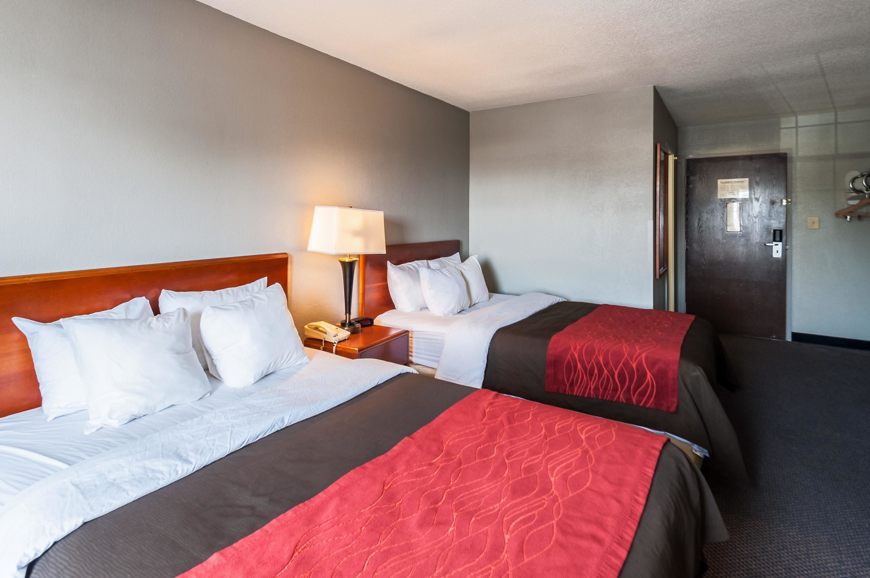 A hotel room with two beds, a nightstand with a lamp, and a door to the bathroom.