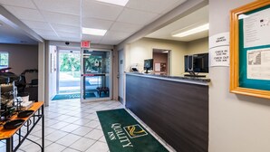 A hotel reception area with a check-in counter, a guest services board, and a reception desk.