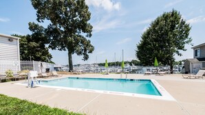 A rectangular pool with a white deck, surrounded by lounge chairs and umbrellas, with a white fence and trees in the background.