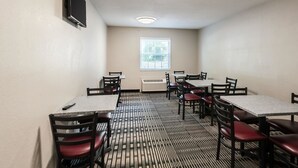 A conference room with a patterned carpet, tables, chairs, a mounted TV, a window with blinds, and an air conditioning unit.