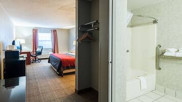 A hotel room with a bed, desk, chair, and a shower area.