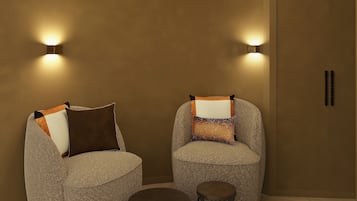 Dos sillones con cojines, una mesita redonda y dos luces fijadas a la pared en una habitación con un diseño de techo circular.
