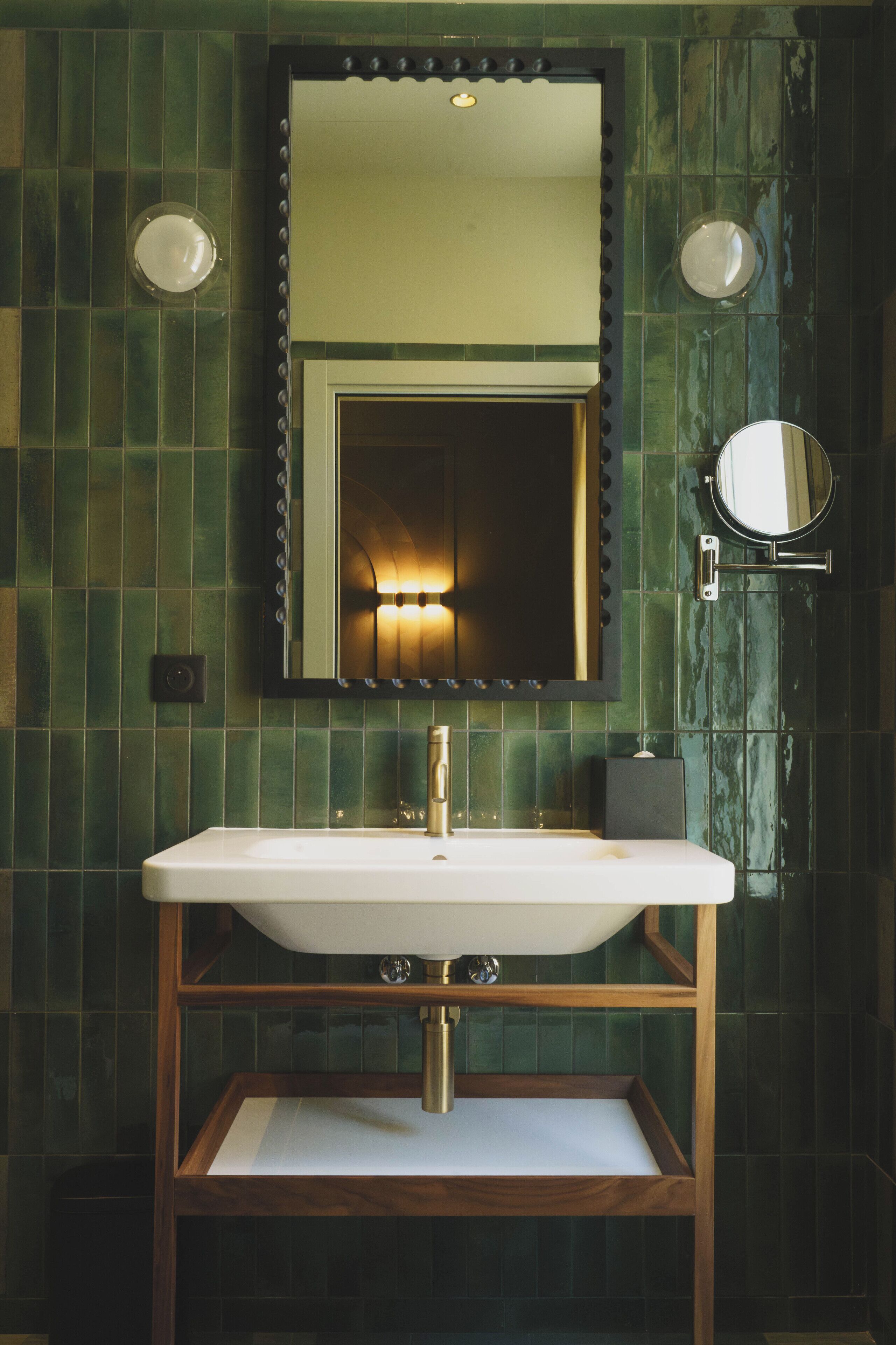 Un baño con lavamanos blanco, tocador de madera y espejo con luces.