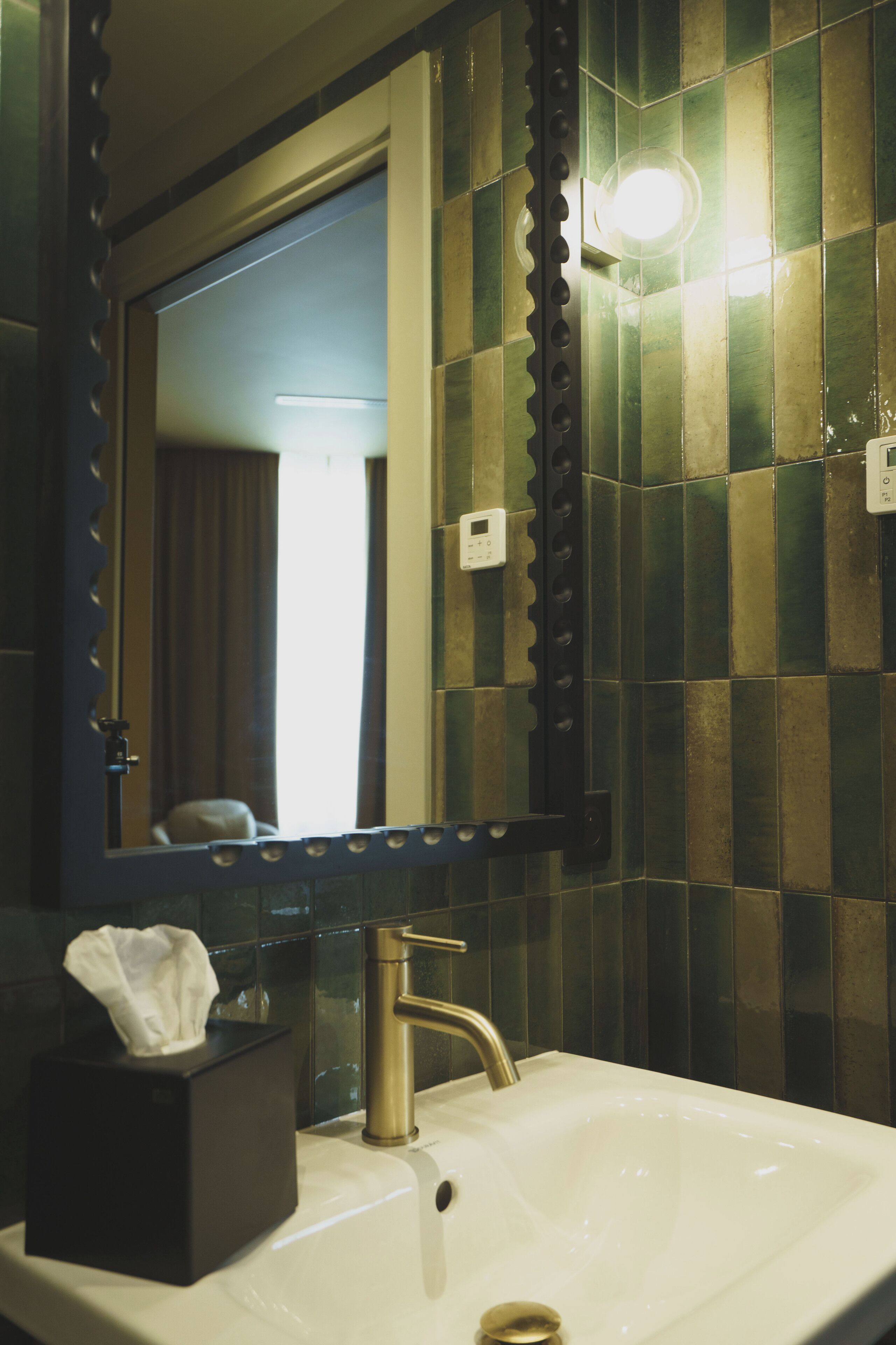 A bathroom with a white sink, a gold faucet, and a mirror with a decorative frame.