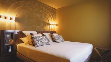 A neatly made bed with white bedding and patterned pillows, a wooden headboard with built-in lighting, and a small bedside table with a lamp.