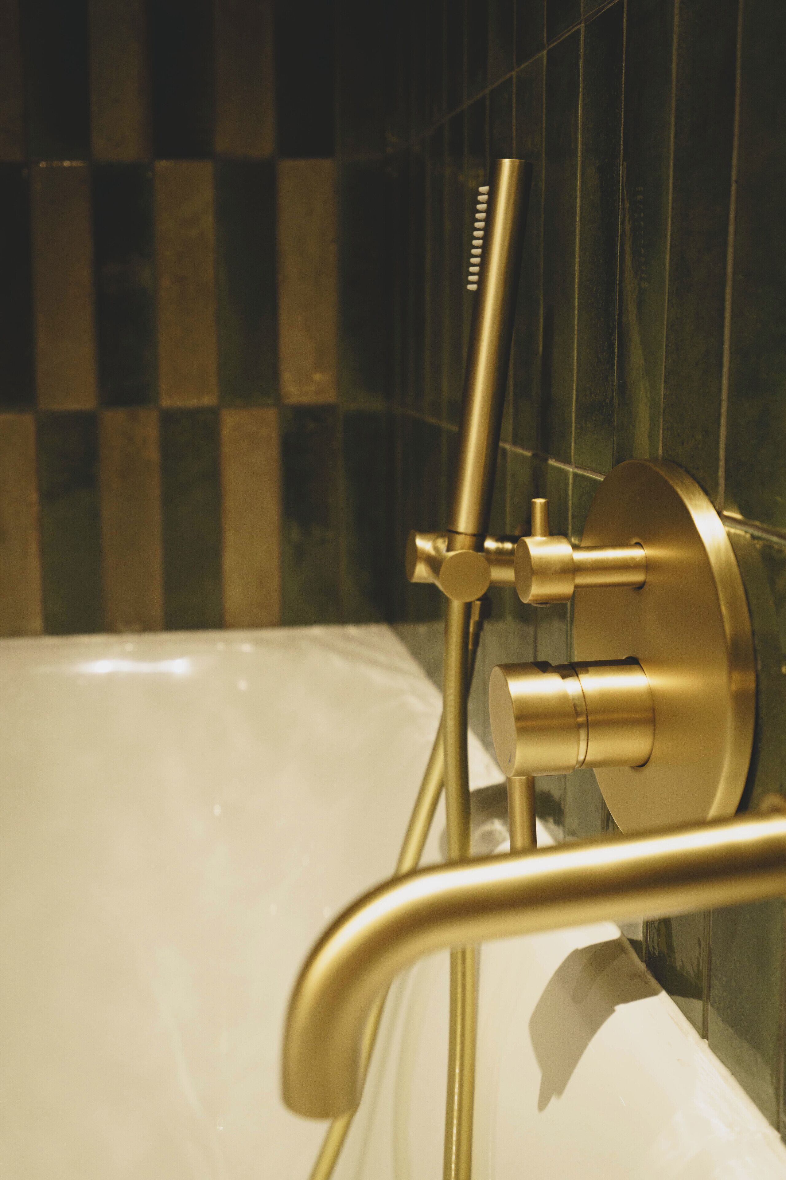 Un baño con bañera, cabezal de ducha dorado y pared de baldosas a cuadros.