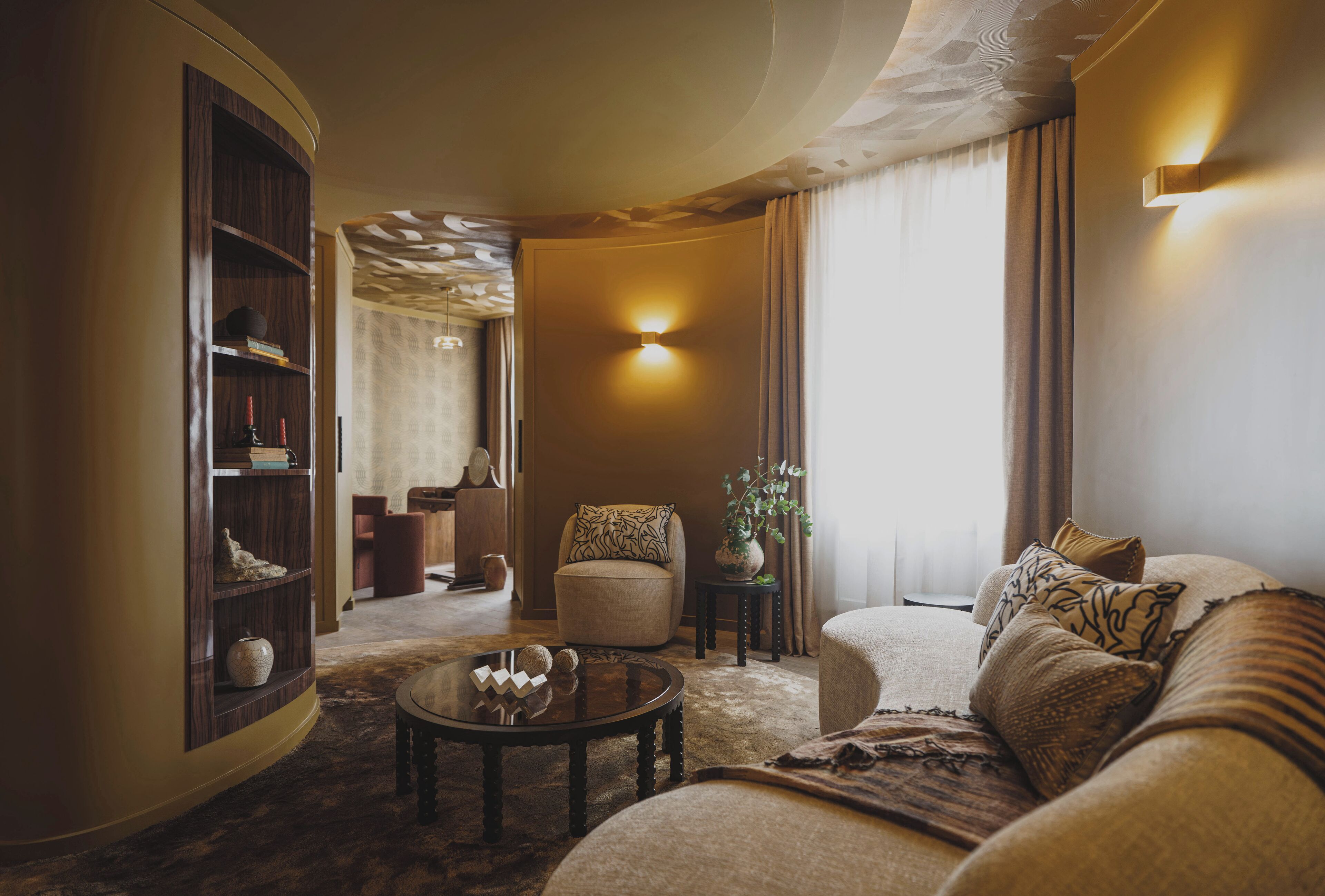 A cozy living room with a round coffee table, a sofa, a bookshelf, and a wall-mounted light fixture.