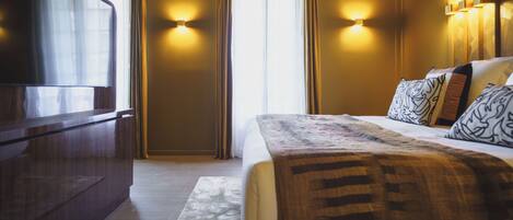 A hotel room with a bed, a TV, and two wall-mounted lights.