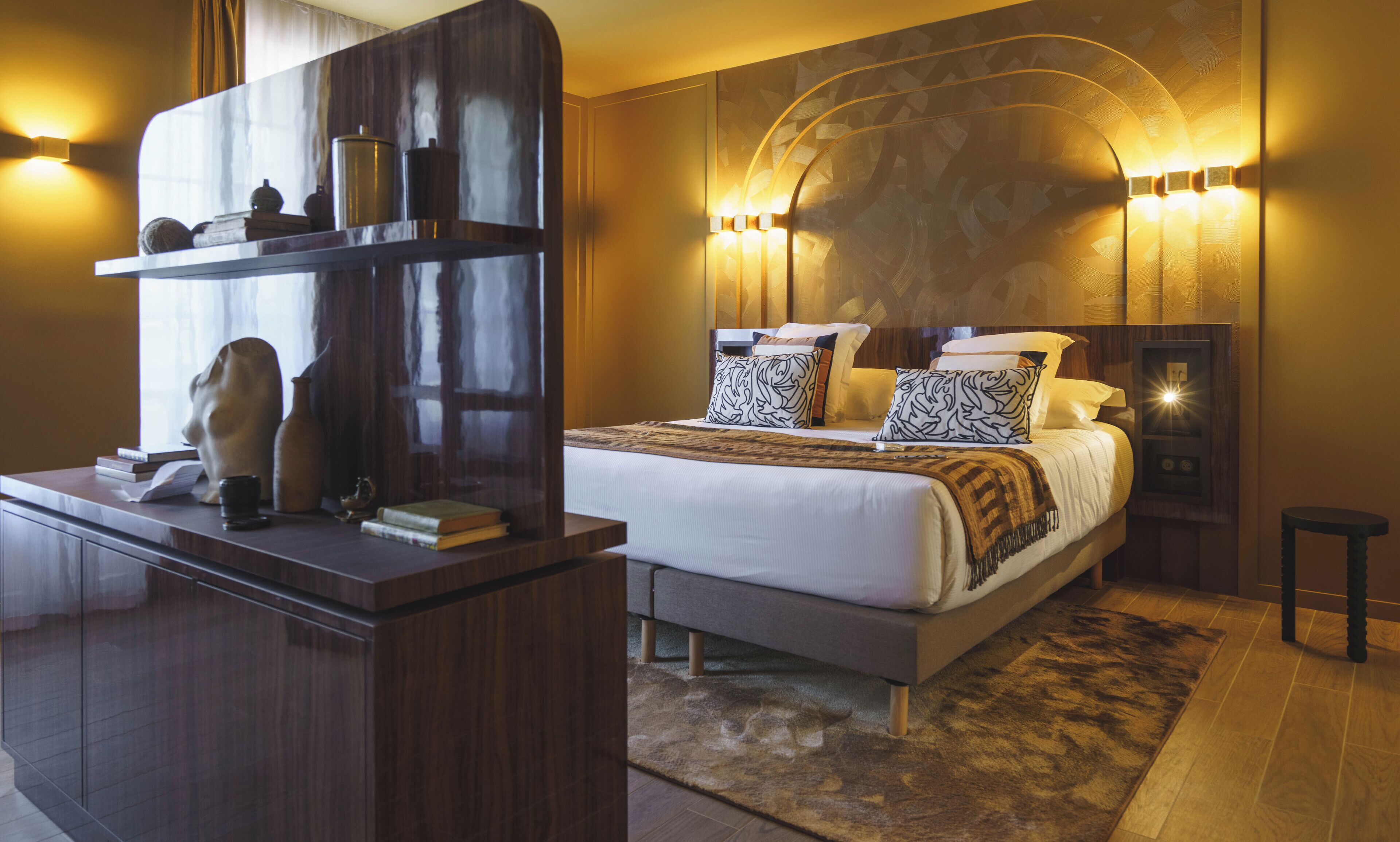 Un dormitorio moderno con una cama grande, mesitas de noche y un escritorio con libros y objetos decorativos.