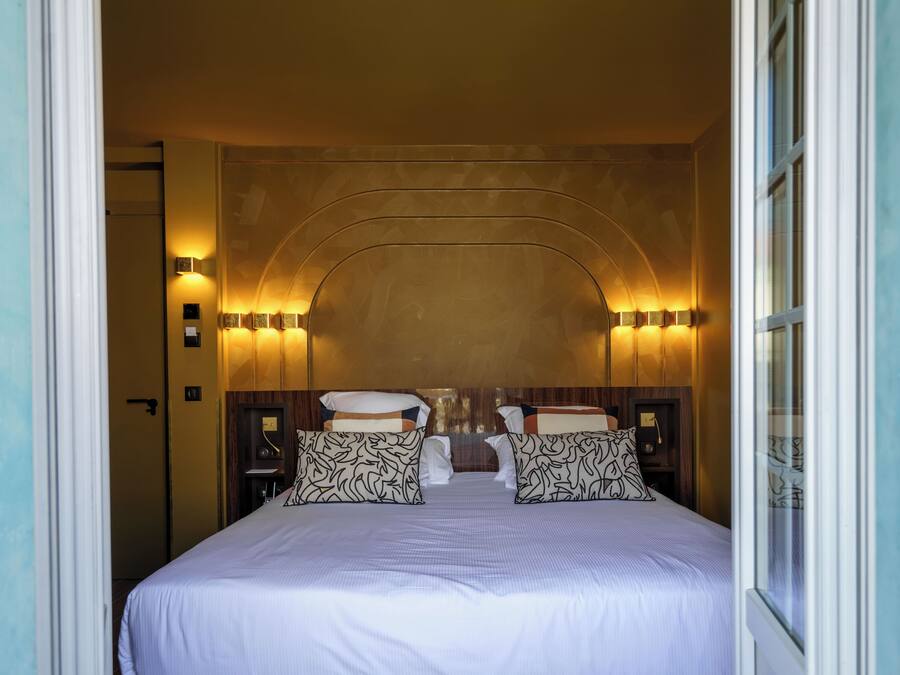 Une chambre d’hôtel avec un grand lit, deux tables de chevet et des lampes fixées au mur.