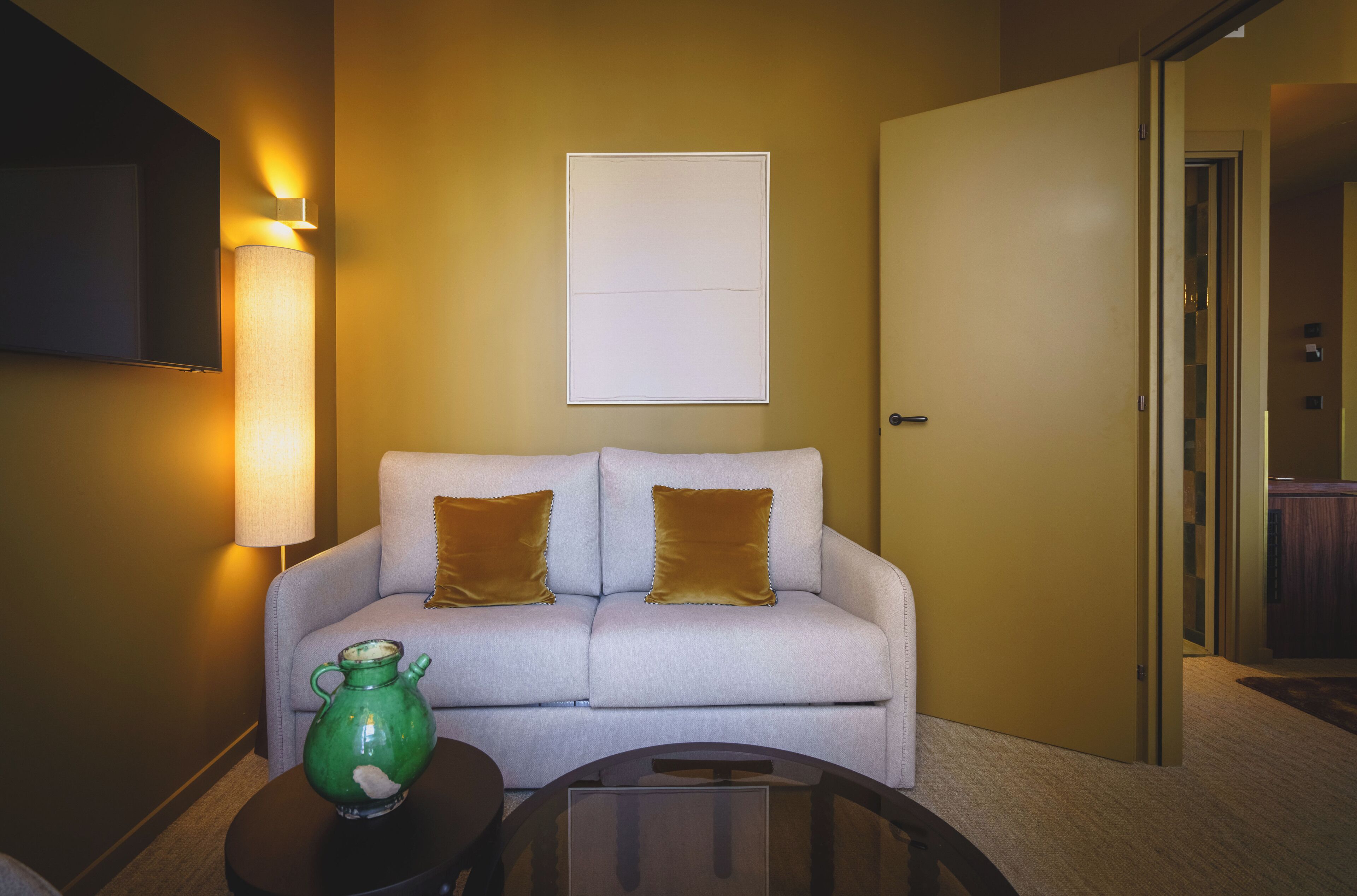 A room with a sofa, a lamp, a vase, and a door.