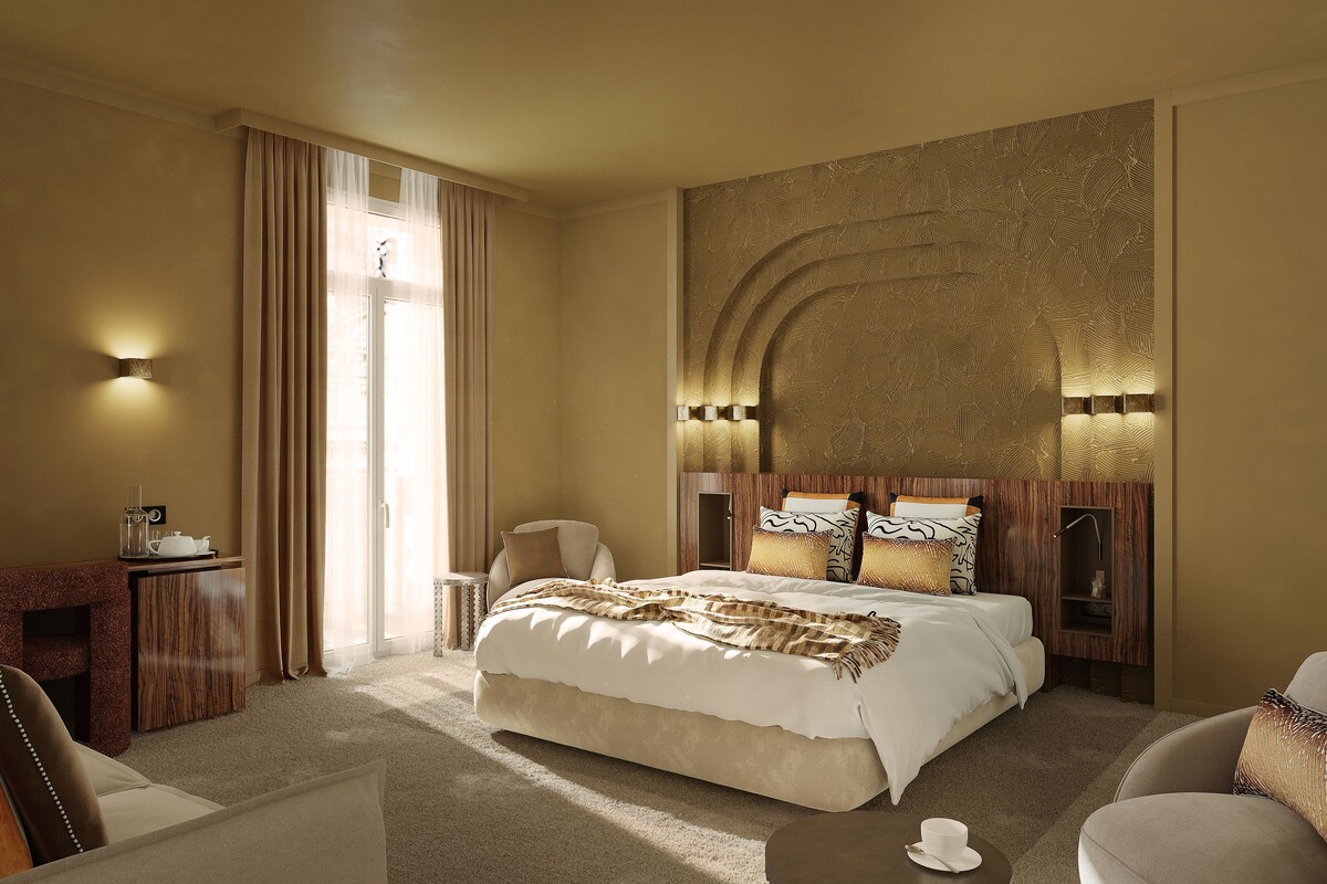 A hotel room with a large bed, a desk with a lamp, a chair, and a large window with curtains.