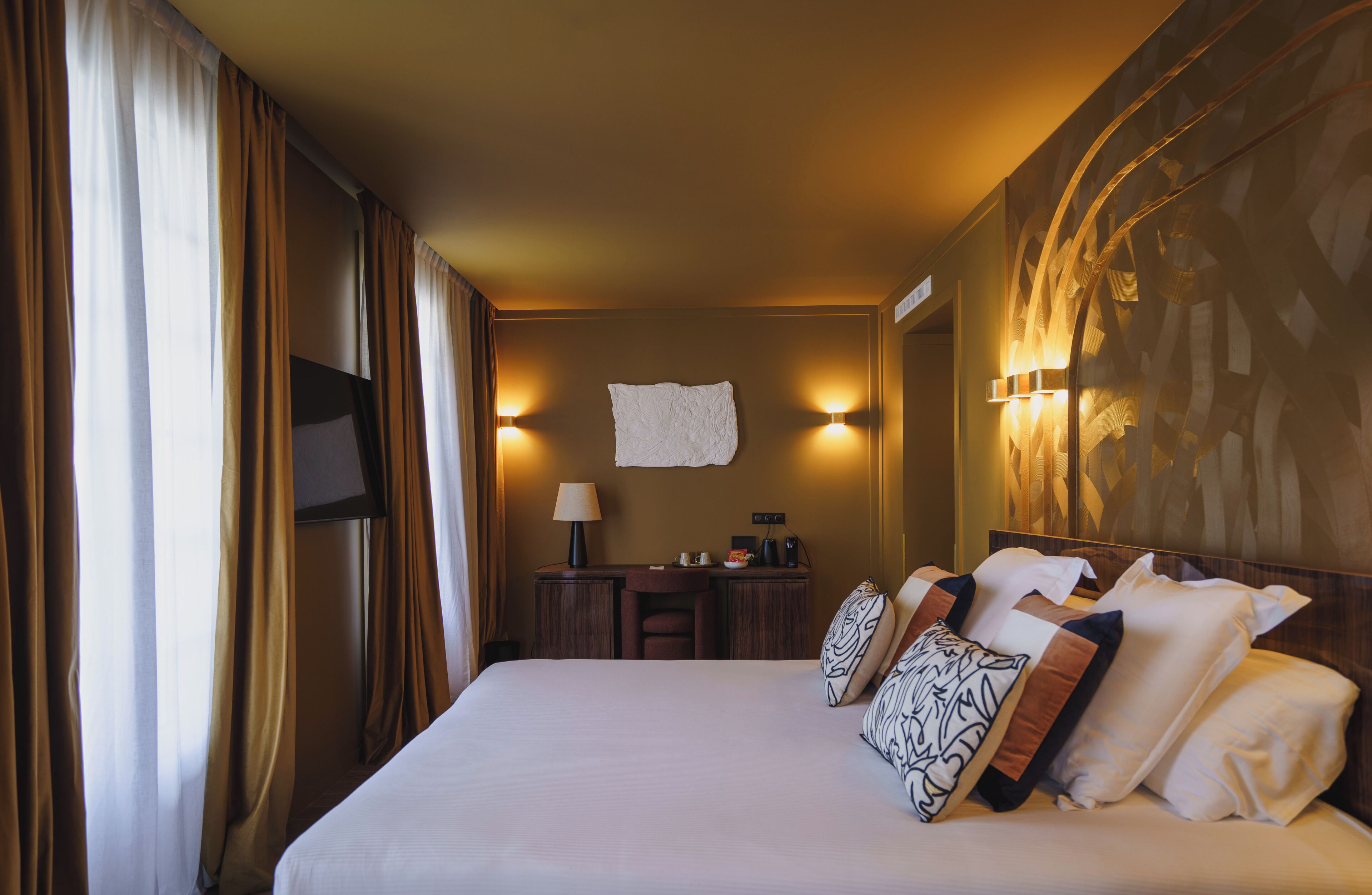 Habitación de hotel con una cama grande, un escritorio, una silla y un televisor montado en la pared.