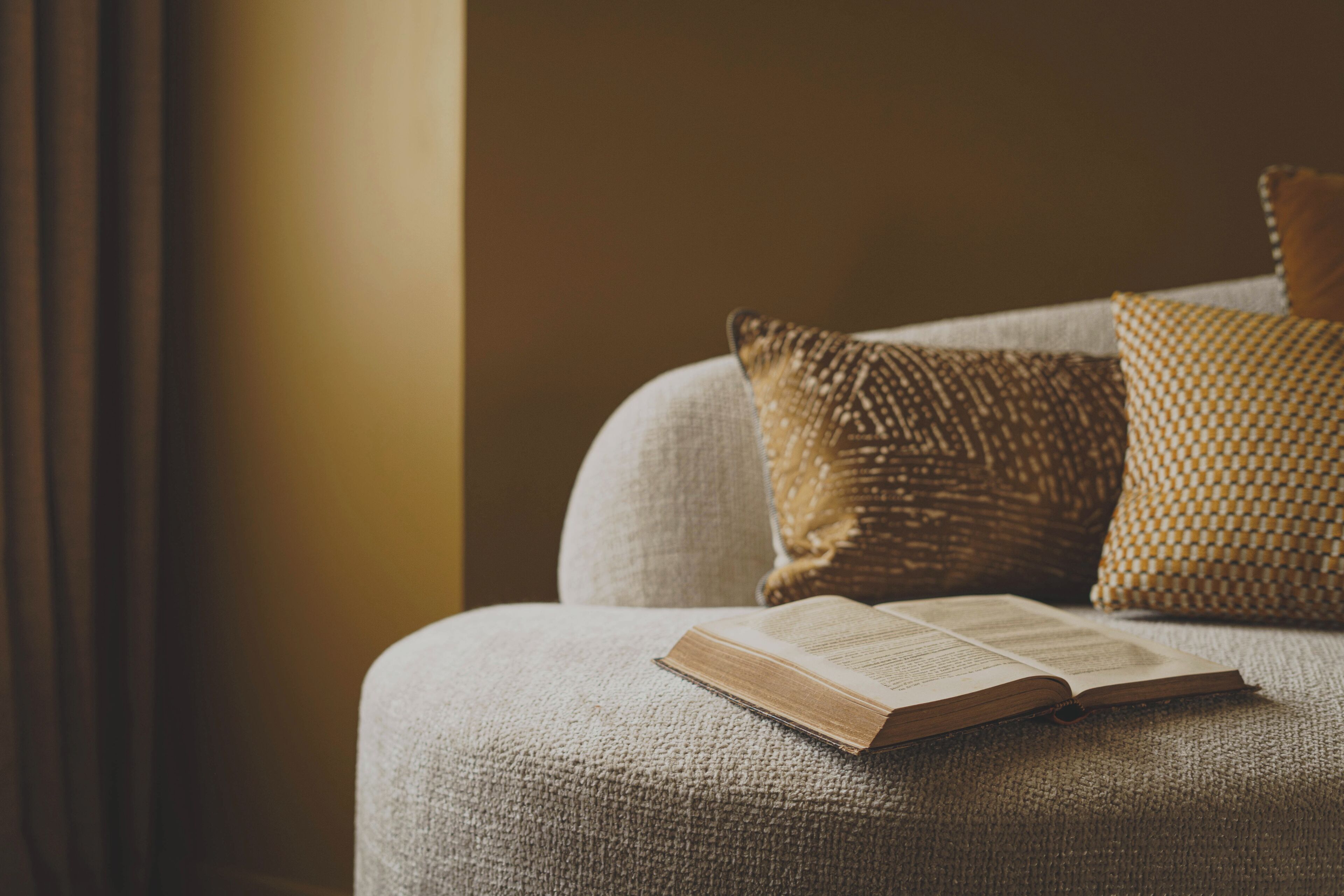 Un libro abierto sobre un sofá con textura y cojines estampados, evocando un espacio acogedor para leer.