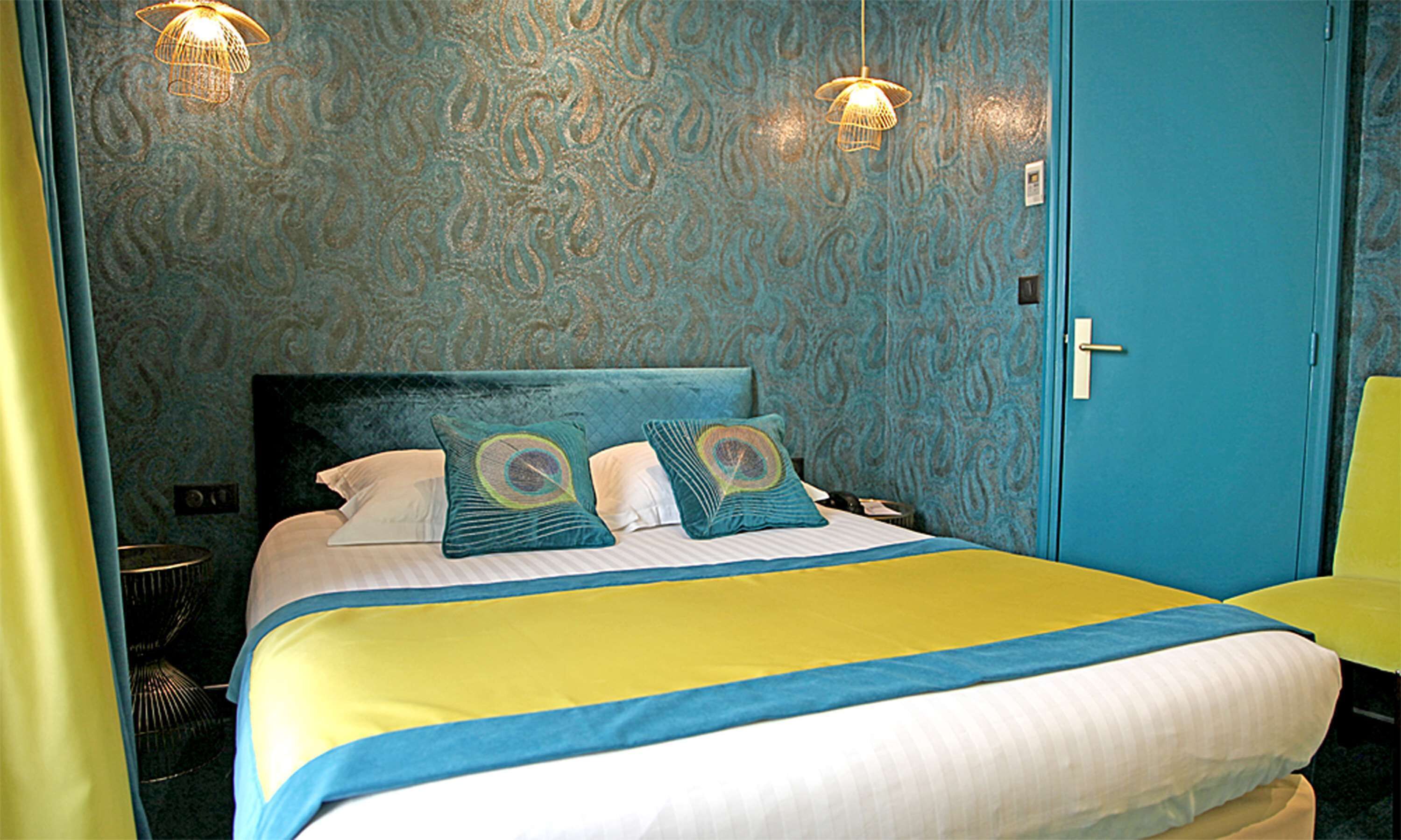 A hotel room with a bed, two decorative pillows, a bedside table, a lamp, and a door.