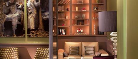 A room with a sofa, a chair, a bookshelf, and a painting.