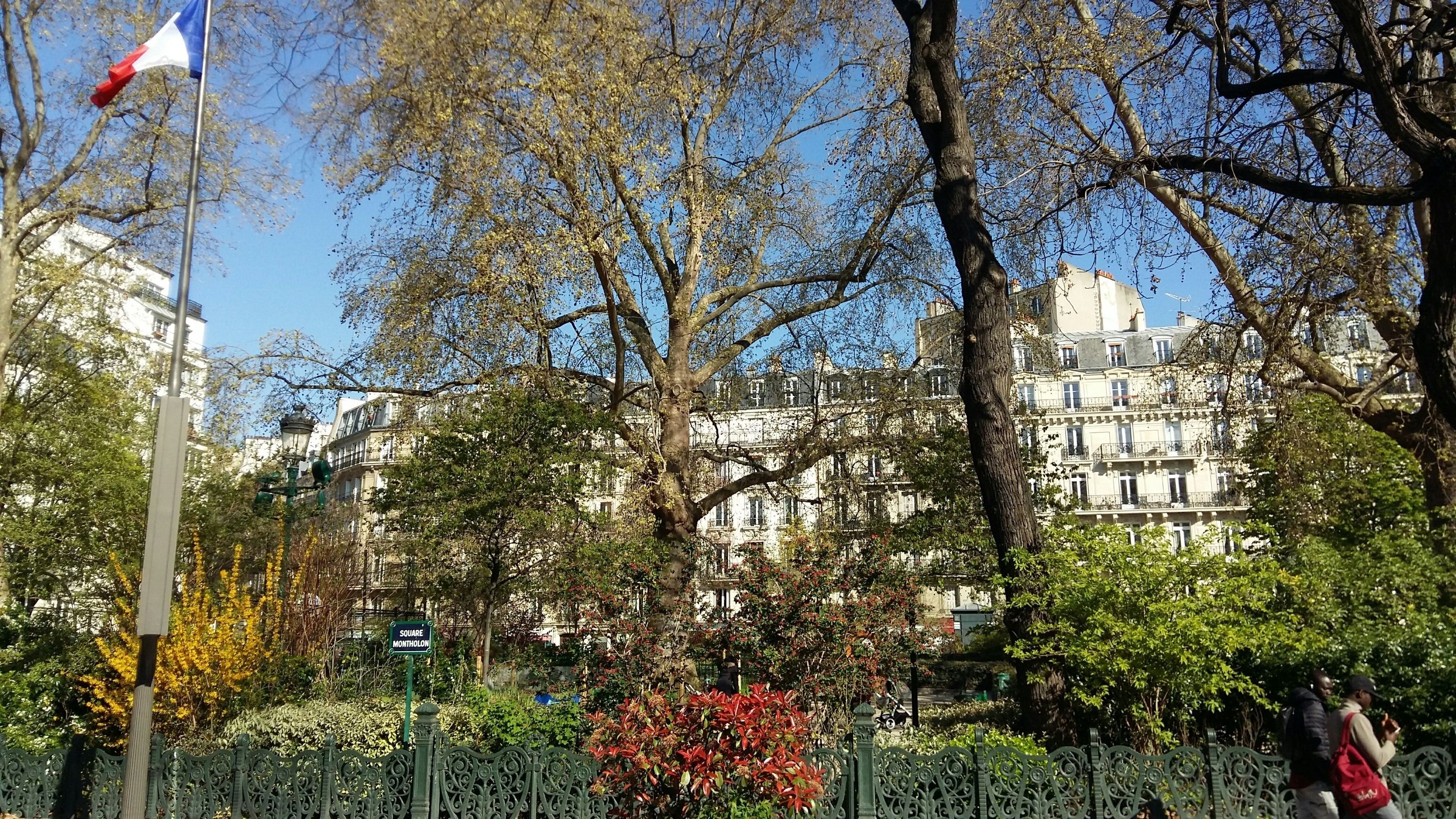 Un parc avec un drapeau, une plaque indiquant « PLACE MONTHOLON », et un immeuble doté de nombreuses fenêtres et de balcons.