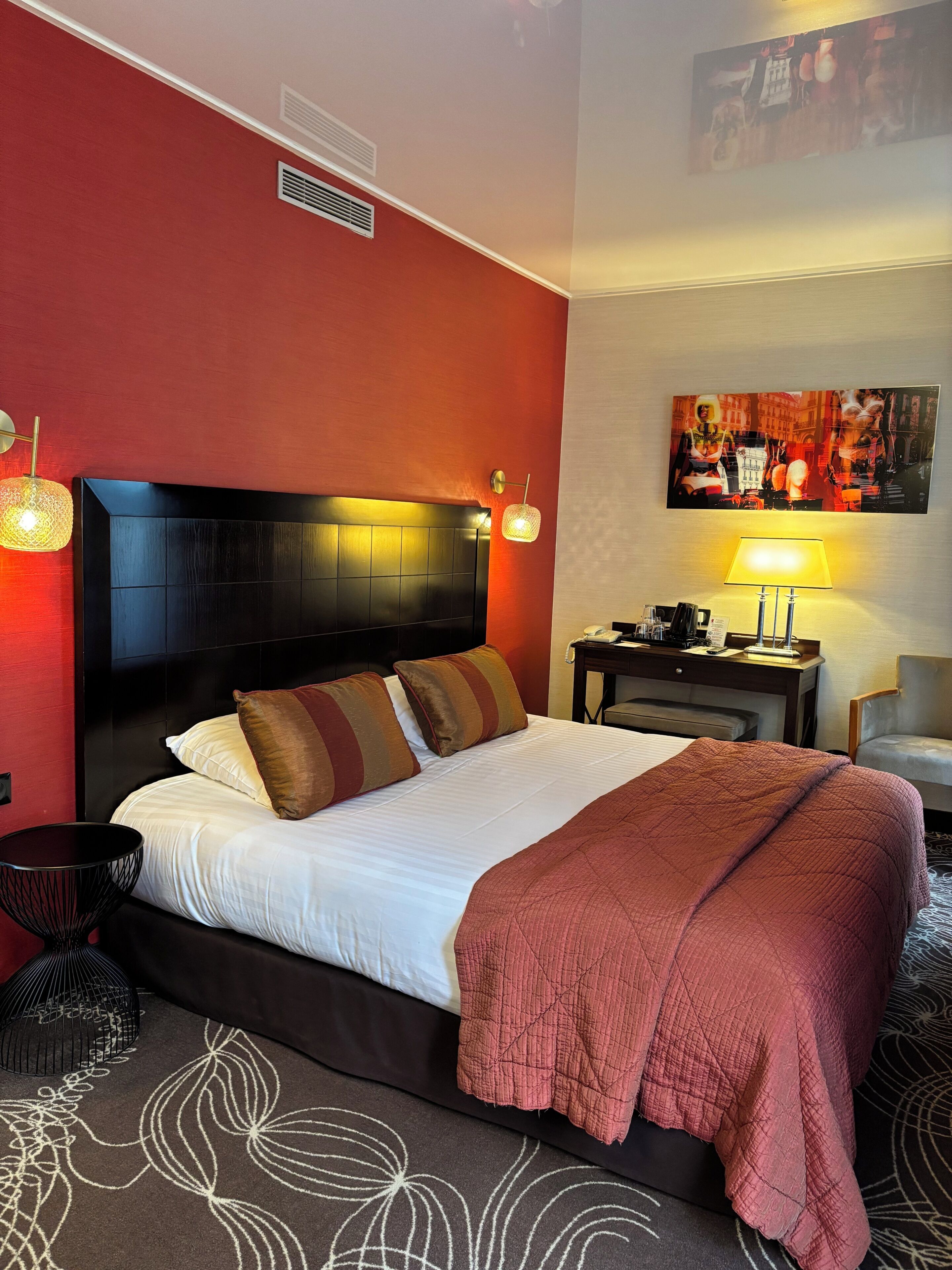 Ein Hotelzimmer mit einem großen Bett, einem Nachttisch, einer Lampe und einem Gemälde an der Wand.