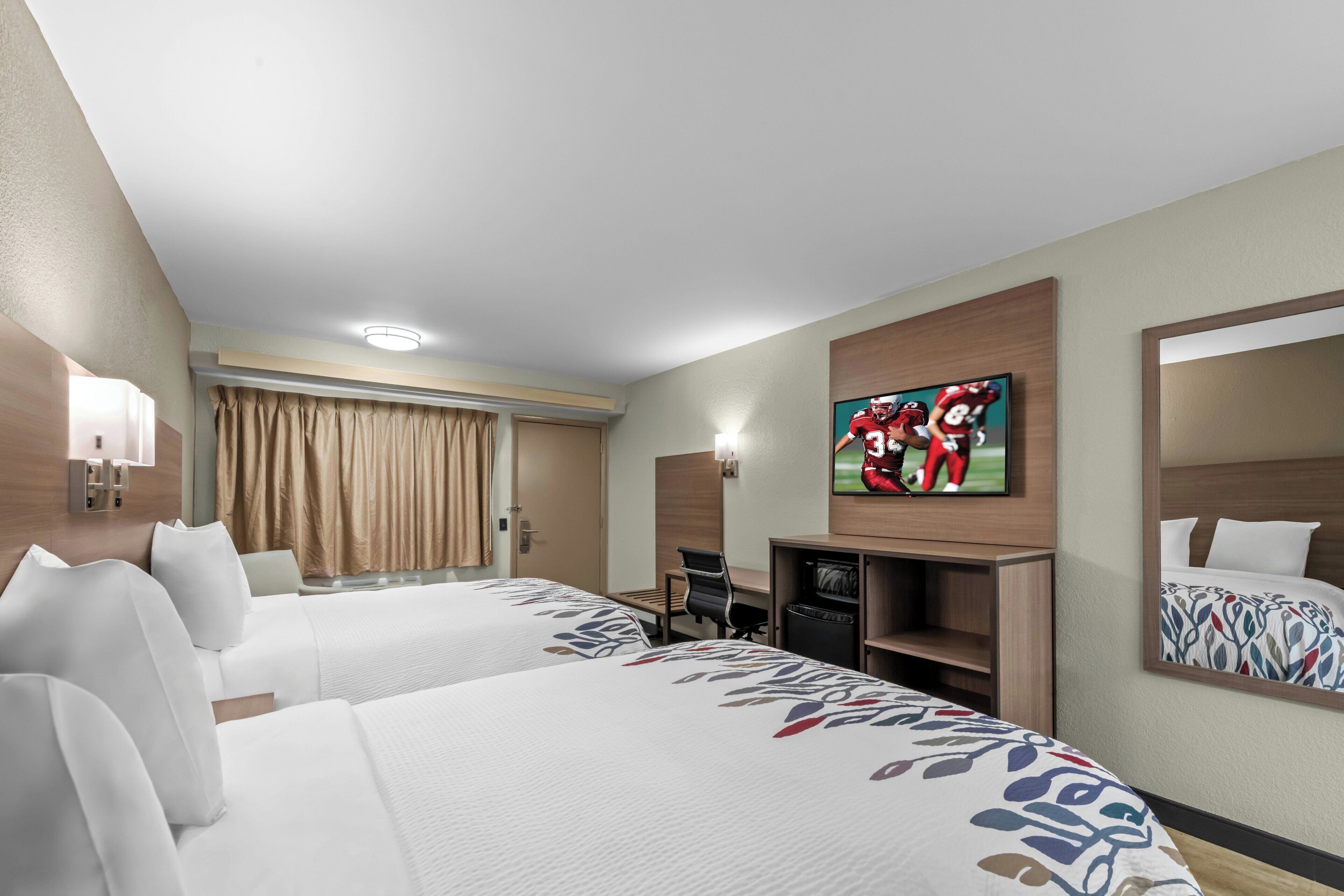 Quarto de hotel com duas camas, televisão, escrivaninha e espelho.