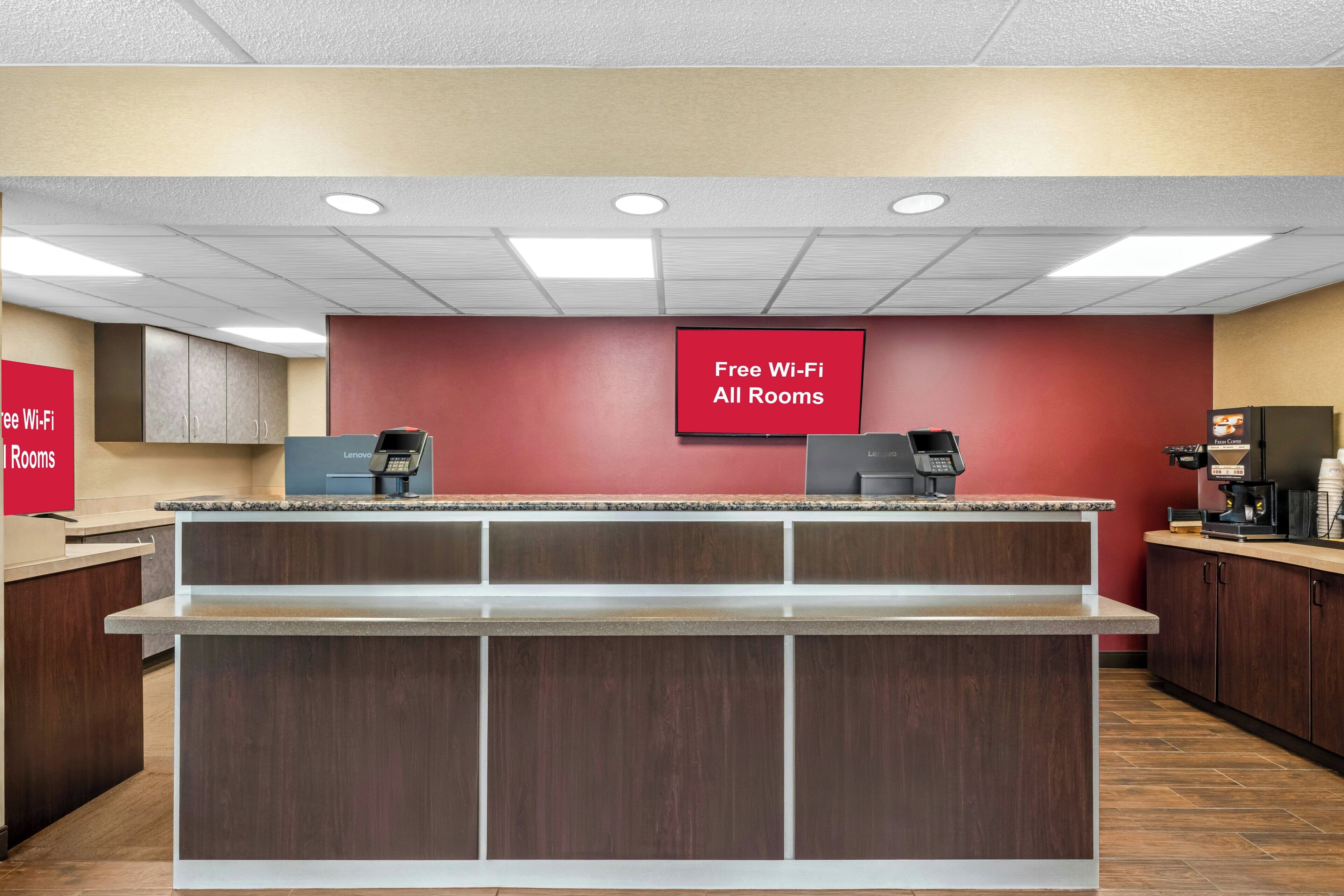 A hotel lobby with a reception desk, a coffee machine, and a sign indicating free Wi-Fi in all rooms.