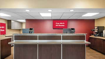 A hotel lobby with a reception desk, a coffee machine, and a sign indicating free Wi-Fi in all rooms.