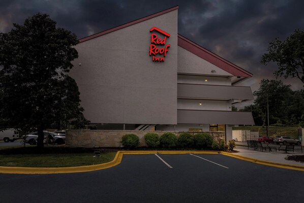 Un Red Roof Inn con un diseño arquitectónico moderno, destacando su techo rojo y un estacionamiento con espacios delimitados.