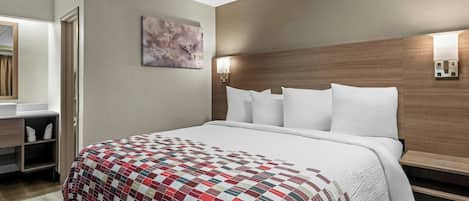 A hotel room with a large bed, a bedside table, a mirror, a wall-mounted light, and a painting.