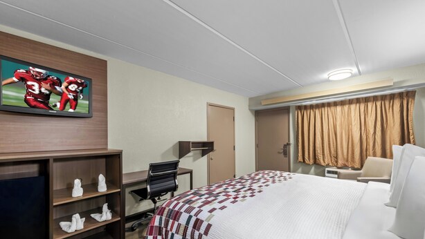 A hotel room with a bed, a desk, a chair, a television, and a window with curtains. - Red Roof Inn Asheville - Biltmore West (Asheville)