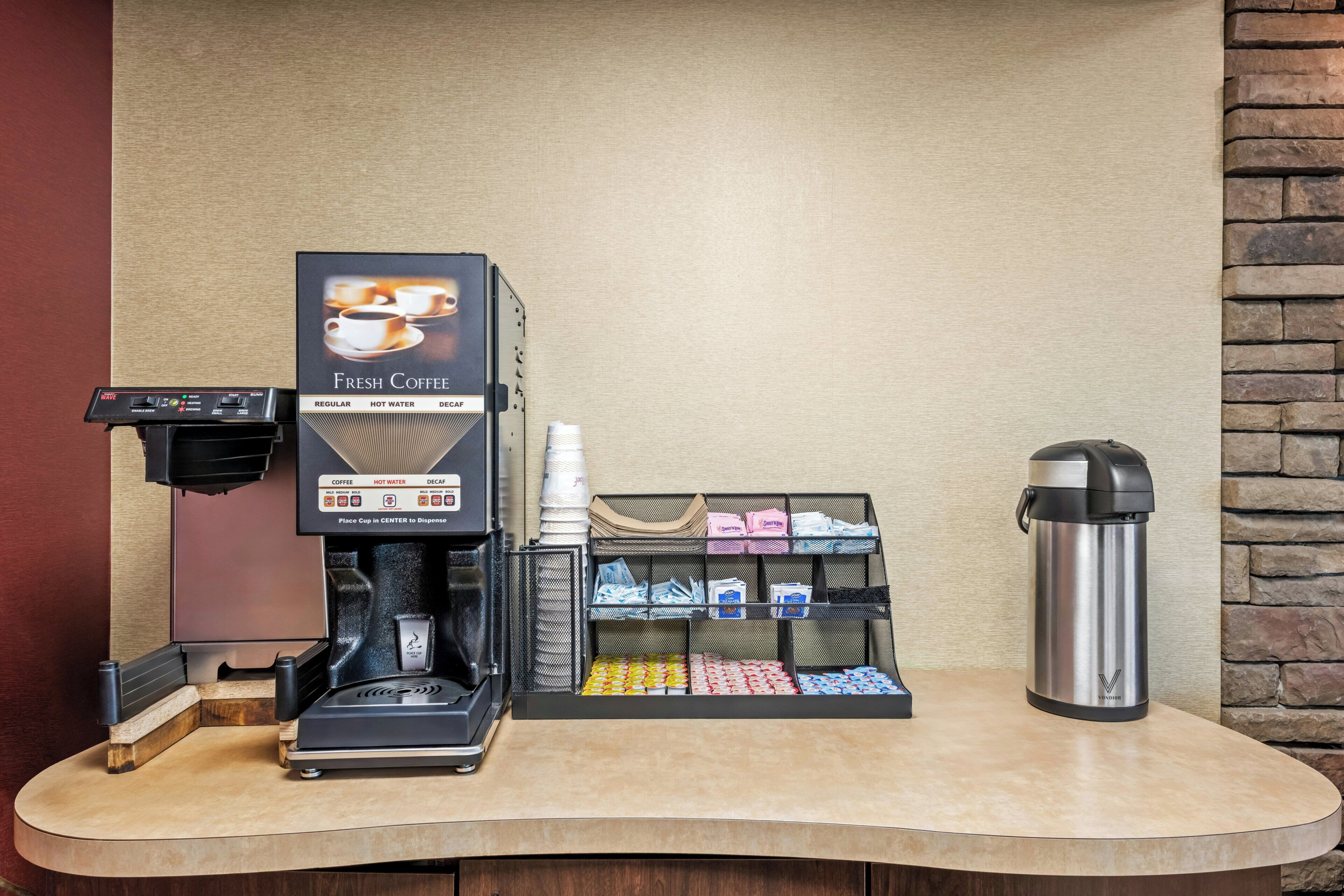 En kaffemaskin med en hållare för kaffekoppar, en dryckesdispenser och en termos på en bänk.