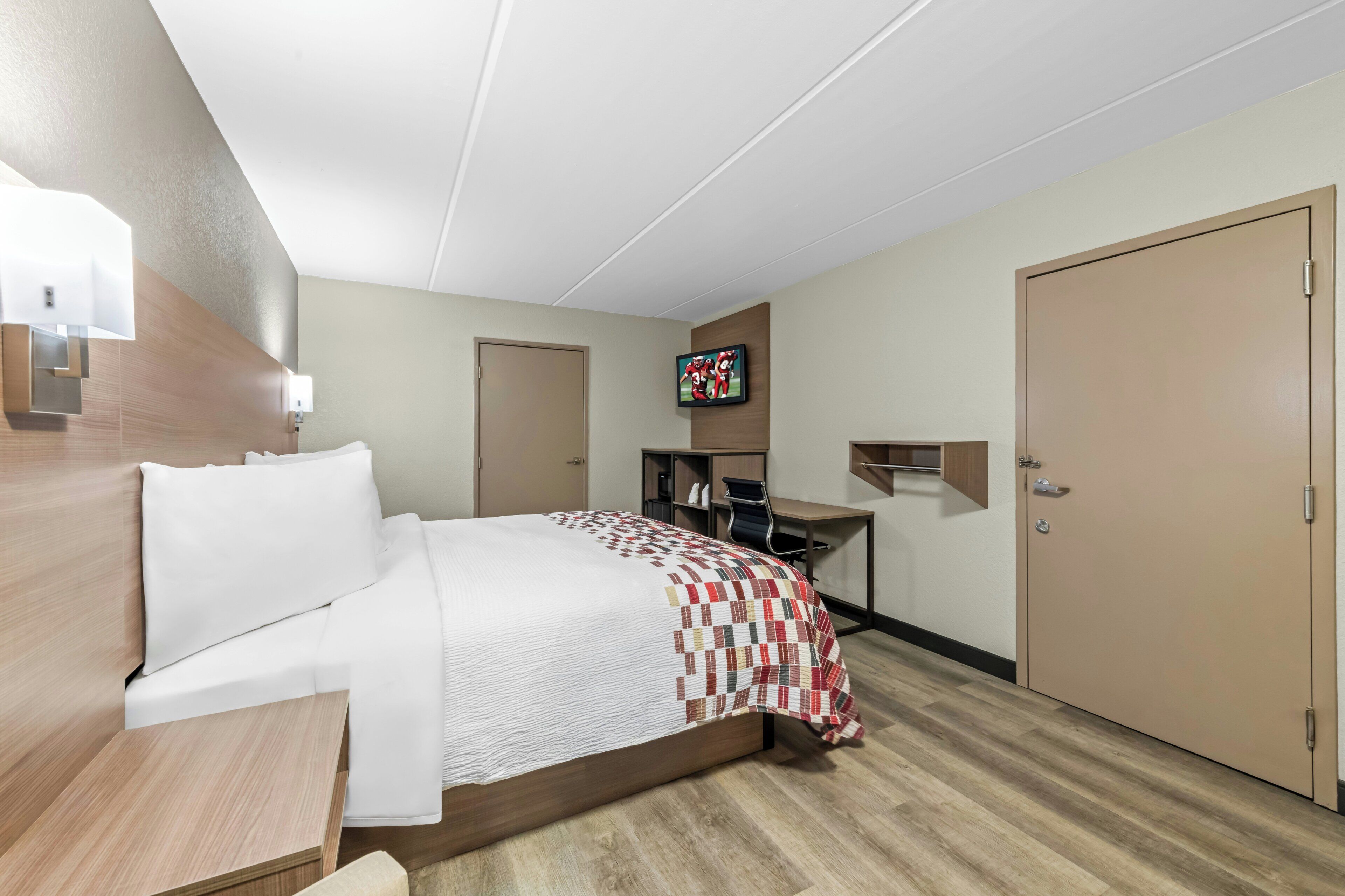 A hotel room with a bed, a desk, a television, and a wardrobe.