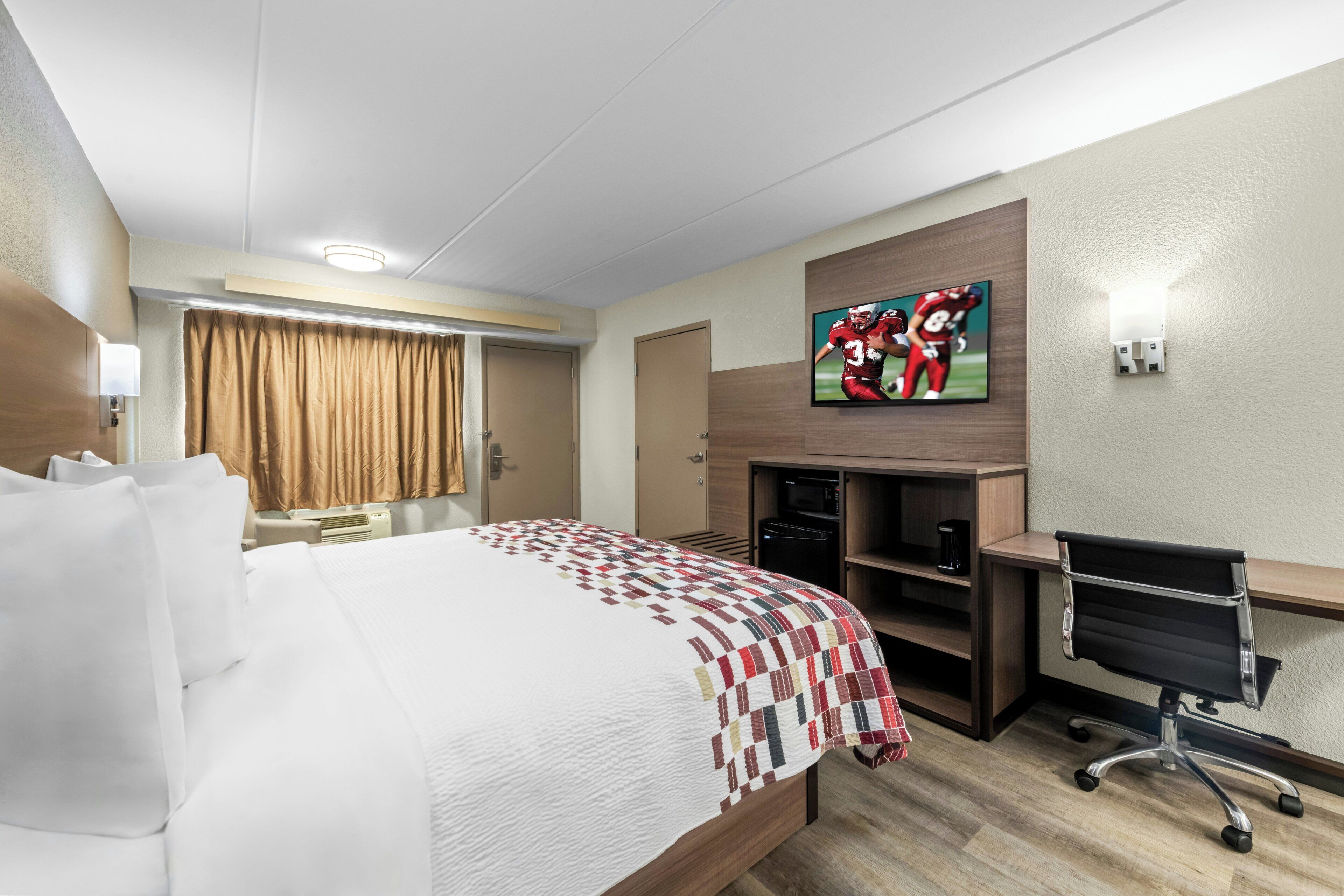 A hotel room with a bed, a desk, a television, and a minibar.