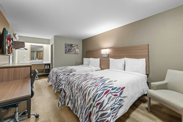 A hotel room with two beds, a desk, a chair, a TV, and a bathroom.